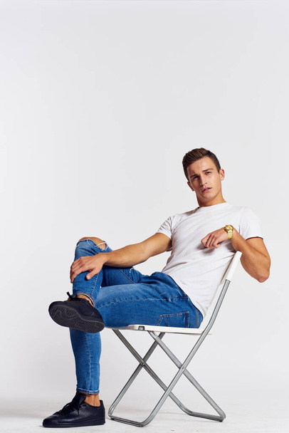Ein Mann in Jeans und T-Shirt sitzt auf einem Stuhl vor hellem Hintergrund - Foto, Bild