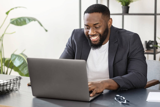 Happy african american man using laptop work study in office - Foto, Imagen