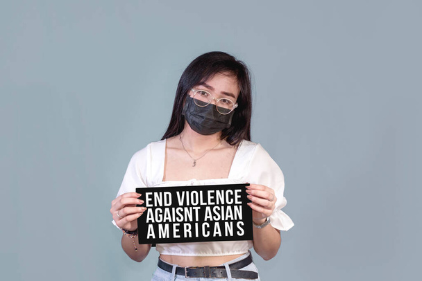 Молодая филиппинка в маске держит знак преступления на почве ненависти. Простой фон. - Фото, изображение