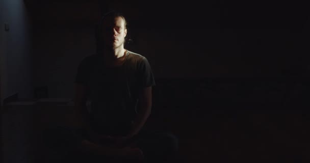 Porträt eines Mannes, der im Lotus Asana sitzt und allein meditiert, im dunklen Raum mit schwarzem Hintergrund. Umfassender ruhiger Yogi, der Yoga-Meditation in Innenräumen praktiziert. Ruhe Ruhe Ruhe Wellness  - Filmmaterial, Video