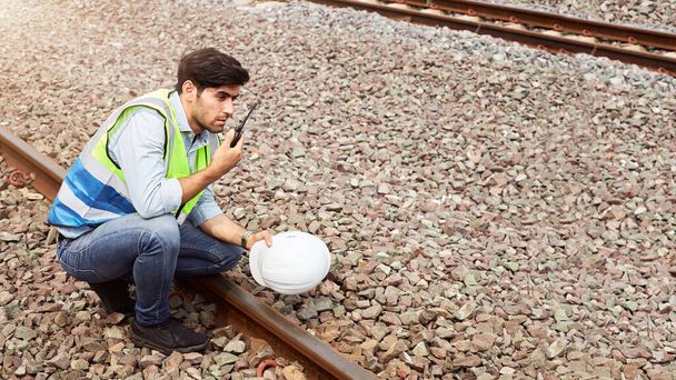 Úspěšní specialisté na logistiku železnic nebo vlakoví inženýři držící přilby a nosící bezpečnostní vesty stojící venku na kolejích mají vysílačku, která kontroluje připravenost práce. - Fotografie, Obrázek
