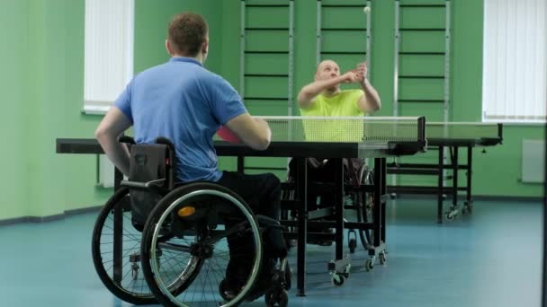 Egy tolószékes férfi pingpongozik. Fogyatékos emberek asztaliteniszeznek. A fogyatékkal élők rehabilitációja. Paralimpiai sport. - Felvétel, videó