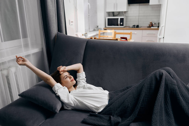 жінка лежить на дивані в кімнаті відпочиває на сірій простій кухні на фоні
 - Фото, зображення