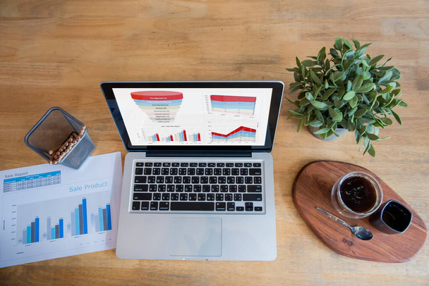 Офисный ноутбук бизнес-график финансовых документов и график на деревянном столе с чашкой кофе. Плоский ноутбук лежал на рабочем столе. Нет людей бизнес-график макет графика на рабочем месте бизнеса - Фото, изображение