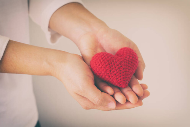 Las mujeres usan camisa de punto con la mano sosteniendo el corazón rojo. Concepto de amor, esperanza, feliz día de San Valentín, salud, donación de órganos, seguro médico, Día Mundial del Corazón, Día Nacional del Donante de Órganos, Día Mundial de la Salud Mental. - Foto, Imagen