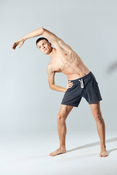 athlete with inflated arm muscles bent over to the side on a gray background exercise  - Zdjęcie, obraz