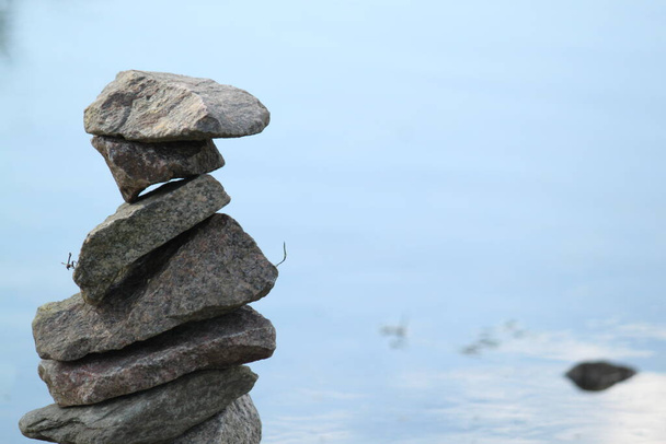 torre construida de piedras apiladas una encima de la otra en el borde de un estanque, fondo azul con espacio para el texto - Foto, Imagen