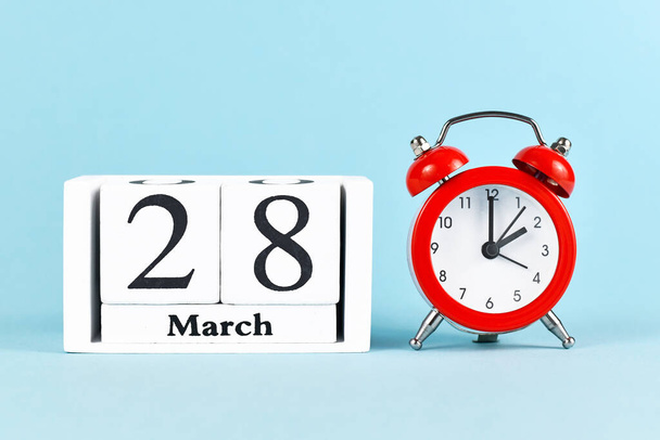 Concept for time change for daylight saving summer time in Europe on March 28th with red alarm clock and calendar on blue background - Foto, Imagem