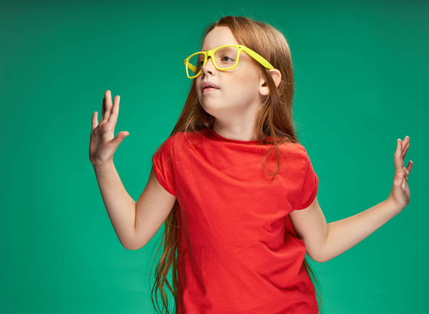 mignonne fille aux cheveux rouges lunettes jaunes émotions studio fond vert - Photo, image
