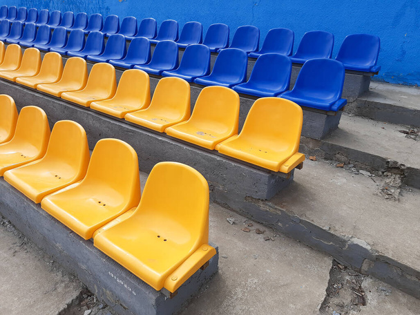Пустые ряды с синими и желтыми сиденьями на стадионе - Фото, изображение