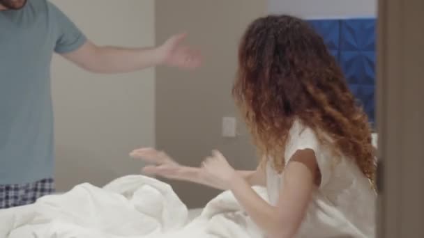 Στιγμιαία φωτογραφία ενός νεαρού Καυκάσιου ανδρόγυνου με πιτζάμες να μαλώνουν στην κρεβατοκάμαρα πριν τον ύπνο, γυναίκα να παραπονιέται, να κατηγορεί και να σπρώχνει τον άντρα, που την κοιτάζει και ζητάει να ηρεμήσει. - Πλάνα, βίντεο