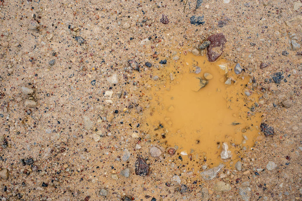 Крупный план латвийской поверхности дороги, где вы можете увидеть яму, заполненную водой, которая была окрашена в желтый цвет из песка, цветные камни хлеба можно увидеть между песком. - Фото, изображение