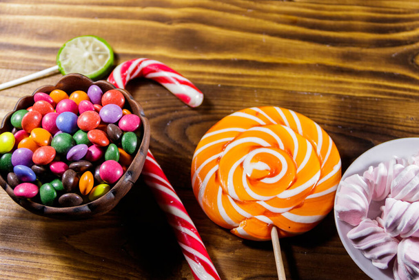 Doces de chocolate coloridos, pirulitos, cana-de-açúcar e marshmallows na mesa de madeira - Foto, Imagem