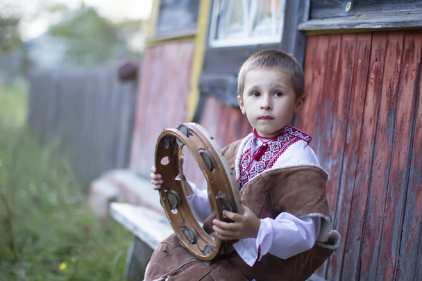 Kleine jongen in Slavische nationale jurk met een etnische tamboerijn. Een Wit-Russisch of Oekraïens kind in een geborduurd shirt met een folkloristisch muziekinstrument. - Foto, afbeelding