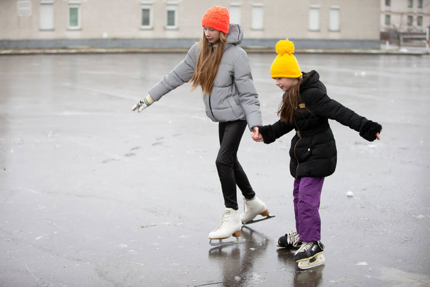 Kinder Schlittschuhlaufen auf der städtischen Eisbahn. Die ältere Schwester bringt der jüngeren das Skaten bei. - Foto, Bild