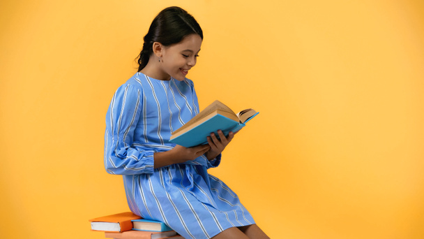 szczęśliwy uczennica w niebieski sukienka czytania książki siedząc na żółty - Zdjęcie, obraz