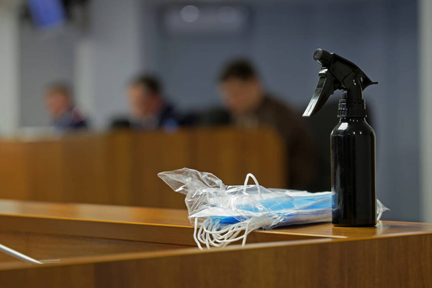 Eine schwarze Sprühflasche mit desinfizierender Flüssigkeit und medizinischen Schutzmasken liegt während eines Geschäftstreffens, einer Verhandlung oder eines Treffens von Beamten auf dem Tisch. Nahaufnahme       - Foto, Bild