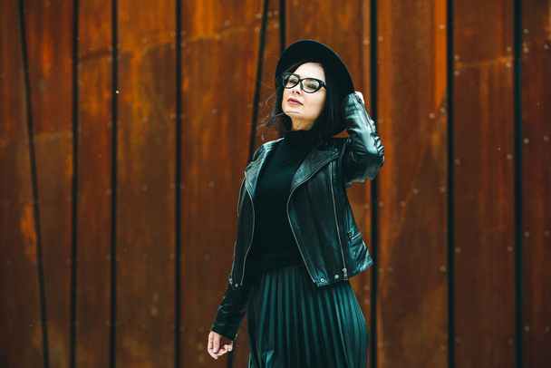 Bella ragazza russa vestita con abiti in pelle nera e occhiali. Stile rock donna europea in background urbano. - Foto, immagini
