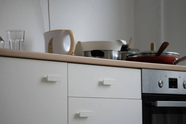 aparato de cocina blanco con un vaso y una tetera, y una sartén roja con una tapa y una olla de metal brillante en la estufa - Foto, imagen