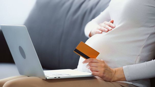 妊娠中の女性がノートパソコンの近くでクレジットカードを持ち - 写真・画像