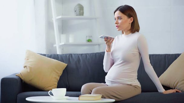terhes nő hangüzenetet küld okostelefonon csésze közelében, és foglalja le a dohányzóasztalon - Fotó, kép