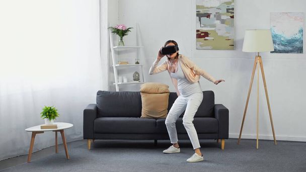 Полный вид беременной женщины, играющей в гарнитуру VR в гостиной - Фото, изображение