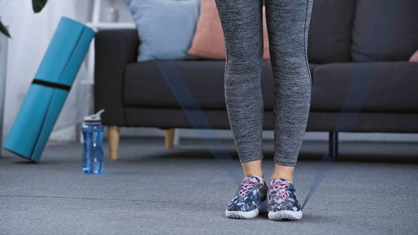 ostříhaný pohled na ženu ve sportovním oblečení cvičení s rozmazaným odbojovým pásem doma  - Fotografie, Obrázek
