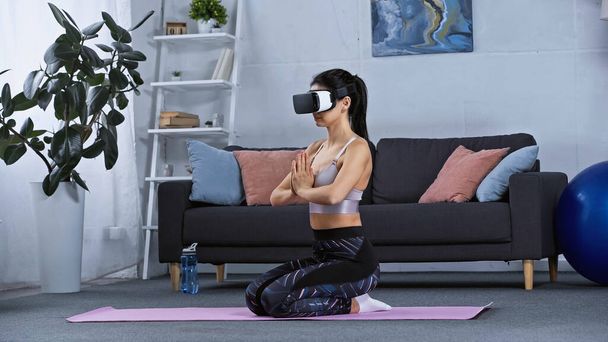 junge Frau in Sportbekleidung und Kopfhörer sitzt auf Fitnessmatte, während sie zu Hause trainiert - Foto, Bild