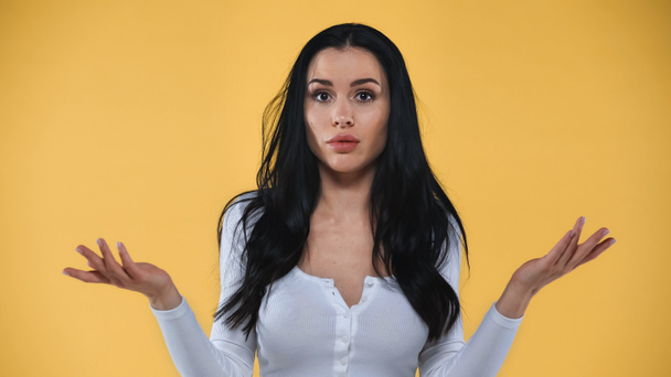 confused woman showing shrug gesture while looking at camera isolated on yellow - Photo, Image