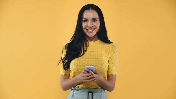 mulher feliz sorrindo para a câmera enquanto conversa no smartphone isolado no amarelo - Foto, Imagem