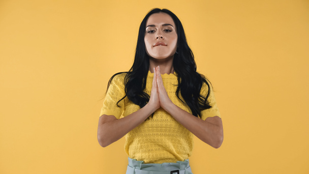 tense woman with praying hands biting lip isolated on yellow - Photo, Image