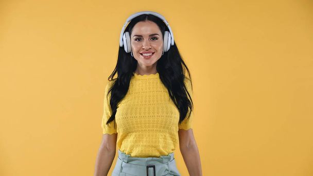 freudige Frau hört Musik in drahtlosen Kopfhörern isoliert auf gelb - Foto, Bild