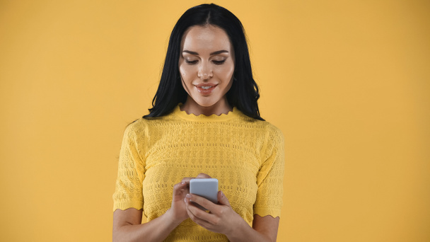 довольна, брюнетка женщина сообщения на мобильный телефон изолированы на желтый - Фото, изображение