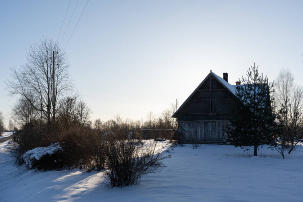egy nagy öreg faház áll egy fehér havas réten, és úgy néz ki, elhagyatott hideg és nedves - Fotó, kép