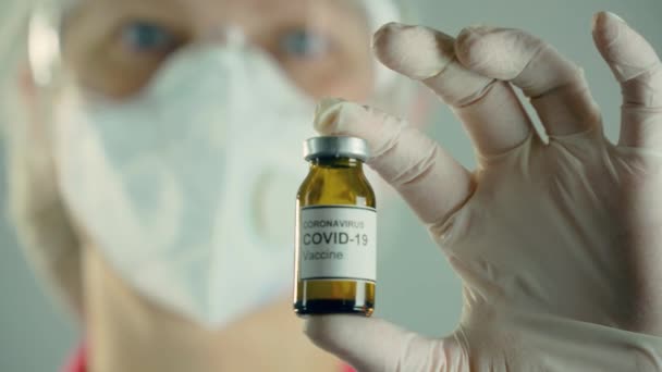 世界的な流行の間に抗コロナウイルスモダニカワクチンでアンプルまたはボトルを保持顔保護マスクの医学研究者を閉じます - 映像、動画