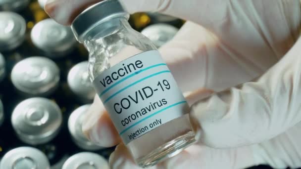 Zavřít koronavirové lahvičky nebo lahvičky s vakcínou v ruce s ochrannými lékařskými rukavicemi ukazujícími farmaceutický průmysl - Záběry, video