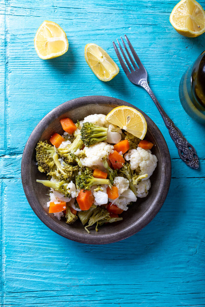 Insalata di broccoli, cavolfiori e carote in ciotola su tavola blu di legno con olio d'oliva e fette di limone.  - Foto, immagini