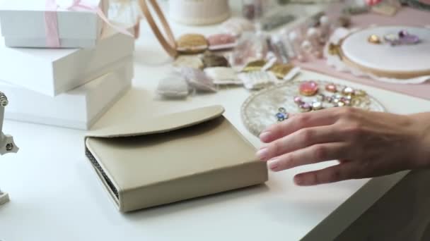 Tasarımcı kumaşta güzel mücevherler ve nakış desenleri yaratır. Bir kadın çalışma masasında oturur ve çalışır, alet çantasını açar. Genç bir girişimci için bir girişim. Evdeki küçük işletme - Video, Çekim