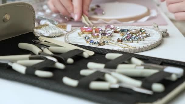 Diseñador crea hermosas joyas con sus manos y patrones de bordado en la tela. Una mujer se sienta en un escritorio y trabaja, abre una caja de herramientas. Una startup para un joven empresario. pequeño b - Imágenes, Vídeo