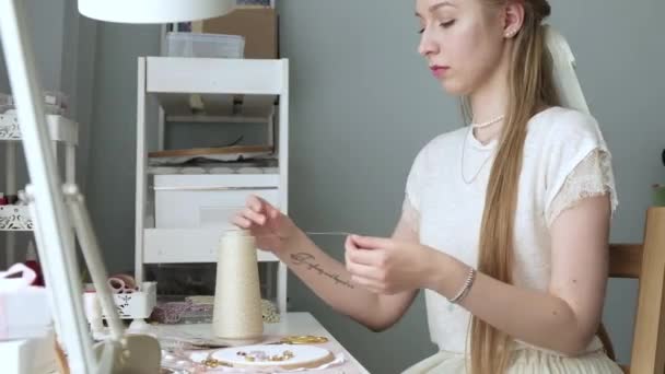 Jonge zelfstandige meester ontwerper vrouw creëert sieraden met handen borduurpatronen op stof. meisje in de kamer zit op het werk en snijdt draad door. Maak handgemaakte sieraden voor online zaken. - Video