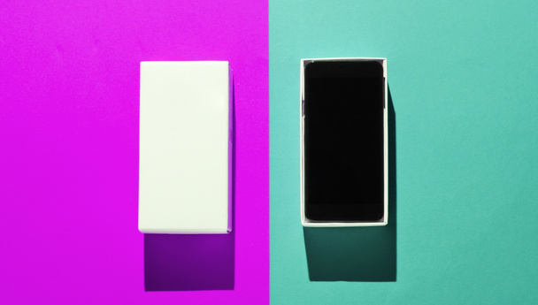 Nuevo smartphone en caja abierta sobre fondo de papel de color. Vista superior, minimalismo - Foto, Imagen