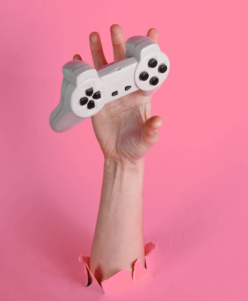 Mano femminile cattura gamepad attraverso strappato carta rosa. Idea creativa minimalista - Foto, immagini