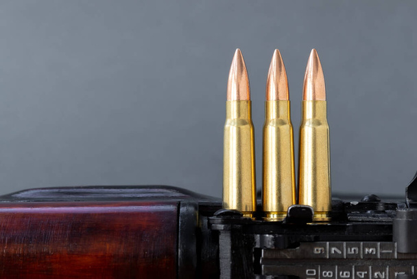Drei Kugeln Kalaschnikow-Sturmgewehr vor verschwommenem grauen Hintergrund. Patronen Kaliber 7,62 für ak 47, Nahaufnahme, selektiver Fokus mit Kopierraum - Foto, Bild