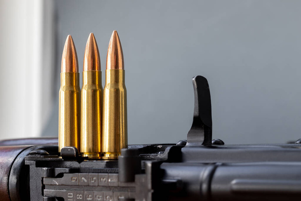 Três balas na espingarda de assalto Kalashnikov contra fundo cinzento desfocado. Cartuchos calibre 7.62 para ak 47, close-up, foco seletivo com espaço de cópia - Foto, Imagem