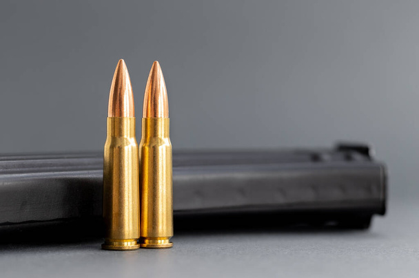 Zwei Kugeln gegen Kalaschnikow-Sturmgewehr-Clip, Magazin auf verschwommenem grauem Hintergrund. Patronen Kaliber 7,62 für ak 47, Nahaufnahme, selektiver Fokus - Foto, Bild