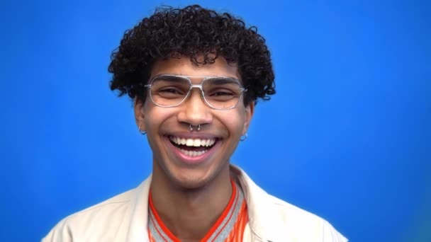 przekłuty Afroamerykanin w okularach śmieje się odizolowany na niebiesko - Materiał filmowy, wideo