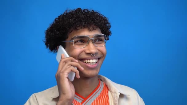 fröhlicher afrikanisch-amerikanischer Mann mit Brille, der auf seinem Smartphone isoliert auf blauem Grund spricht - Filmmaterial, Video