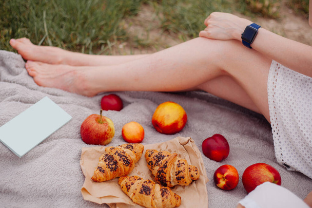 自然の中で夏のピクニック。女の子はマットに座ってクロワッサンとリンゴを食べる - 写真・画像
