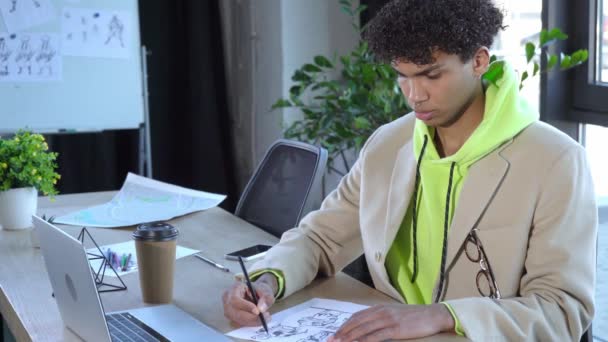 curly african american illustrator drawing character on paper near laptop - Footage, Video