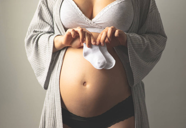 Terhes nő baba zoknit tart a terhes hasa mellett. Babaruha. Anyai terhesgondozás. Anyaság, terhesség, baba-várandósság. A terhesség második trimesztere. Fénymásolási hely - Fotó, kép